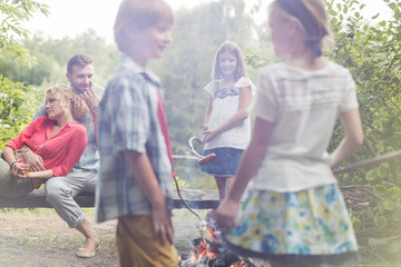 Kids standing at campsite while parents sitting on bench in public park