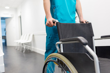 Midsection of nurse pushing wheelchair in hospital corridor 