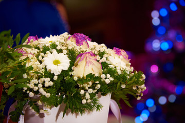 A bouquet of flowers in a box on the background of bright multi-colored bokeh.