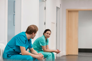 Male and female nurses talking while sitting in corridor at hospital