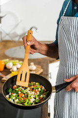 cropped image of middle aged man cooking vegetables on frying pan in kitchen