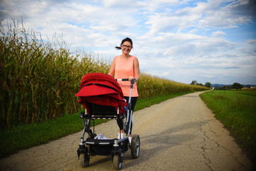 Adorable baby in red stroller in fields with mother. Relax in nature