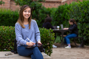 Portrait of young asian american university student working on park bench quad lawn, tablet computer