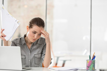 Overworked young businesswoman holding documents while suffering from headache