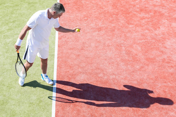High angle view of confident mature man serving on tennis court during match on sunny day