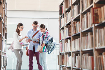 Friends discussing while reading book at library in university