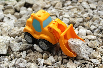 A small orange toy digger picks up gray stones