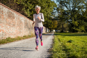 Senior woman running along brick wall in a park