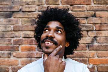 Mid adult man standing in front of brick wall, looking up, smiling