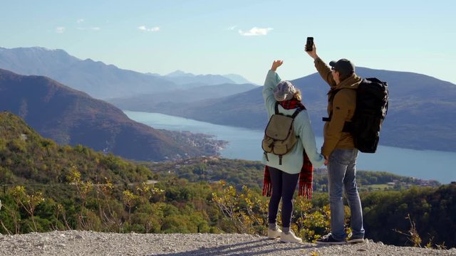 A couple of travelers with a phone waving at the top of a mountain.