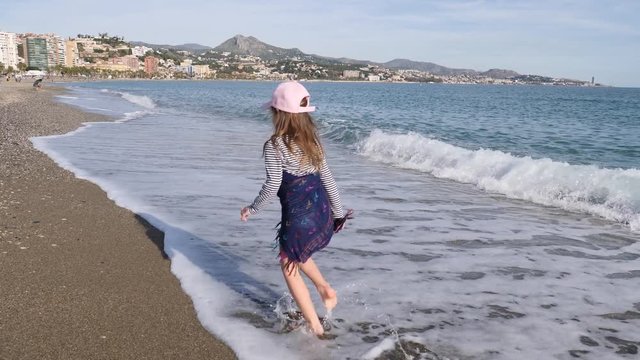 Barefoot little girl kid joyfully running shallow waterline of Malaga beach in december