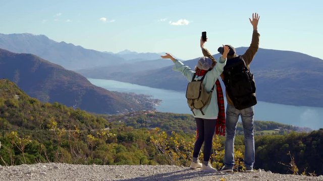 A couple of travelers with a phone waving at the top of a mountain.