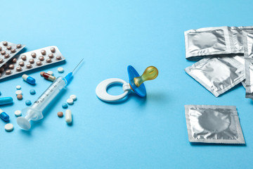 Birth control pills, an injection syringe and condom in a package on blue background. The concept of choosing method of contraception, birth control pills or condom. Baby nipple as symbol of pregnancy