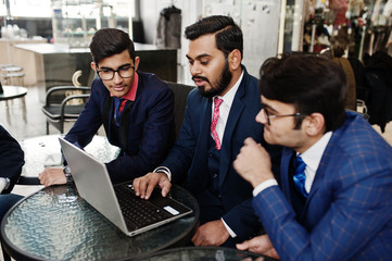 Group of three indian business man in suits sitting at office on cafe and looking at laptop.