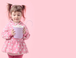 Cute little girl holding small violet bucket of marshmallow.