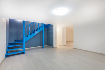 Empty basement room with laminate flooring, high ceiling and deep blue wooden staircase