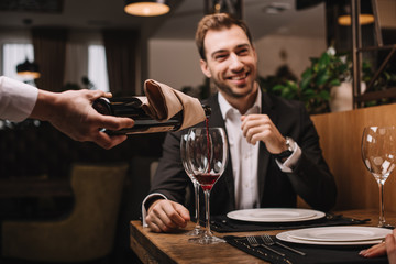 selective focus of attractive man in suit smiling and sitting in restaurant