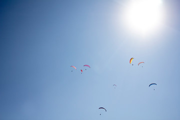 several paragliders on colorful parachutes in a clear blue sky with a bright sun