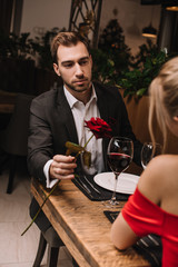 handsome man giving rose to girlfriend while sitting in restaurant