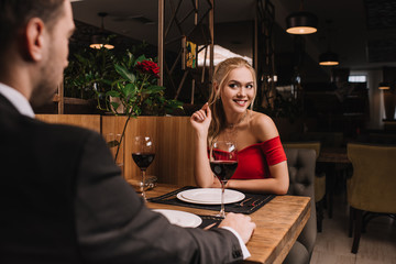 attractive woman flirting with boyfriend while sitting in red dress in restaurant