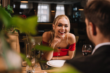selective focus of cheerful girl looking at man and laughing in restaurant