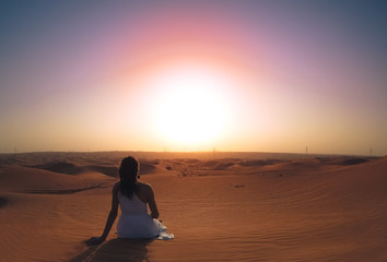 a girl in a dress sits on a hill in the desert and admires the sunset. the view from the back