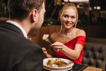 attractive girlfriend feeding boyfriend in restaurant