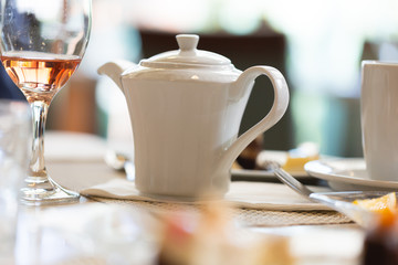 Teapot on table in luxury restaurant next to glass with rose wine
