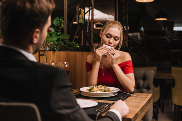attractive blonde woman wiping mouth with napkin near boyfriend in restaurant