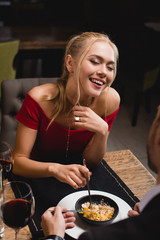 happy woman laughing  near boyfriend while sharing dessert in restaurant