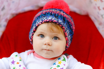 Cute healthy little beautiful baby girl with blue warm hat sitting in the pram or stroller and waiting for mom. Happy smiling child with blue eyes. baby daughter going for a walk with family