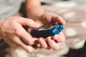 Theme diabetes. A close-up macro plan. Hands of a young Caucasian woman at home in the bedroom on the bed. It uses the technology of an instrument for measuring the level of glucose in the blood