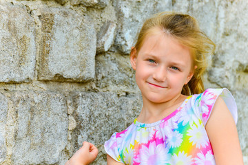Young and beautiful girl posing against a brick wall on the street with a smile in a summer dress.