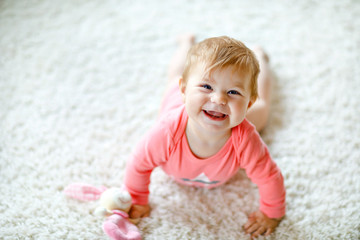 Little cute baby girl learning to crawl. Healthy child crawling in kids room with colorful toys. Back view of baby legs. Cute toddler discovering home and learning different skills