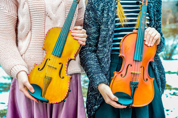 Two girls stand by and hold the violins in their hands.