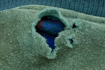 big torn hole on the green fabric of old clothes