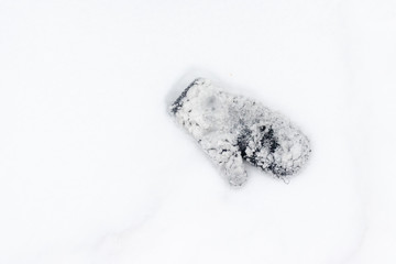 One mitten covered with lots of snow lying on a white snow. Outdoor activity, winter children entertainment and recreation concept, copy space