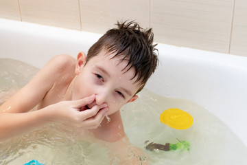 An eight year old boy sitting in bath and pinch the nose ready to dive