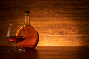 Brandy bottle and glass on wooden background. Cognac on the table