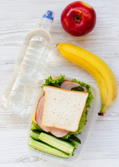 Healthy lunch box with sandwich, fruits and bottle of water on white wooden surface, top view. From above, flat, overhead.