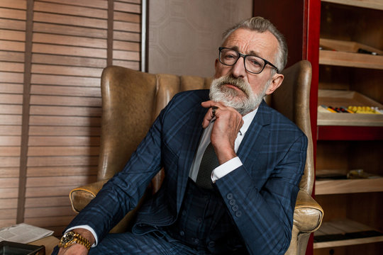portrait of thoughtful senior university professor with grey hair wearing formal clothes, sitting in the sofa indoors, looking back at the past