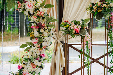 Fototapeta na wymiar Beautiful wedding set up. Area of the wedding ceremony. Round arch, white chairs decorated with flowers, greenery. Cute, trendy rustic decor. Part of the festive decor, floral arrangement.
