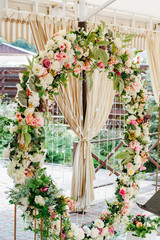 Fototapeta na wymiar Beautiful wedding set up. Area of the wedding ceremony. Round arch, white chairs decorated with flowers, greenery. Cute, trendy rustic decor. Part of the festive decor, floral arrangement.