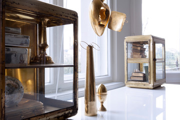 Dekoration in Gold und Messing auf weissem Tisch vor Fenster in heller Altbauwohnung
