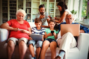 Multi-generation family sitting on sofa and using various