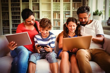 Family using various technologies while sitting on sofa