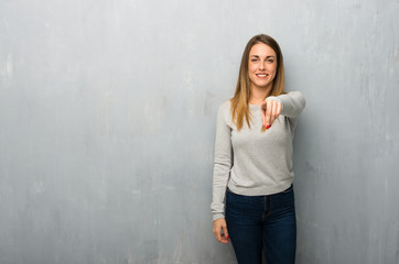Young woman on textured wall points finger at you with a confident expression