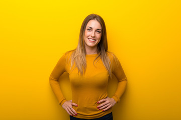 Obraz premium Young woman on yellow background posing with arms at hip and laughing looking to the front