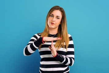 Blonde youn girl making stop gesture with her hand on blue background