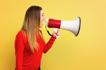 Young blonde woman holding a megaphone on yellow background